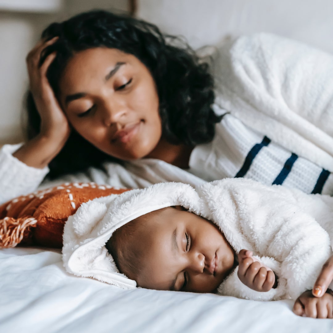 young mother in bed looking at sleeping newborn baby
