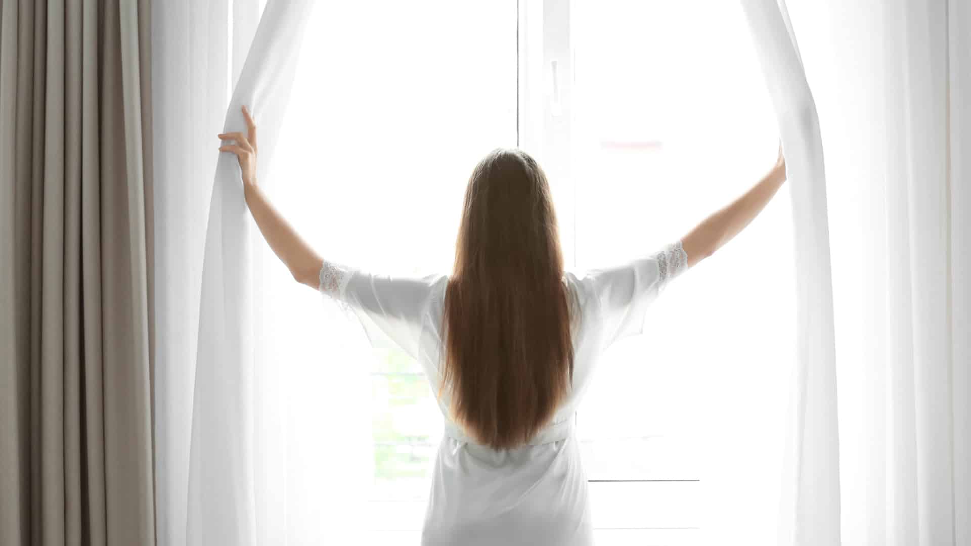 woman opening curtains on a sunny day