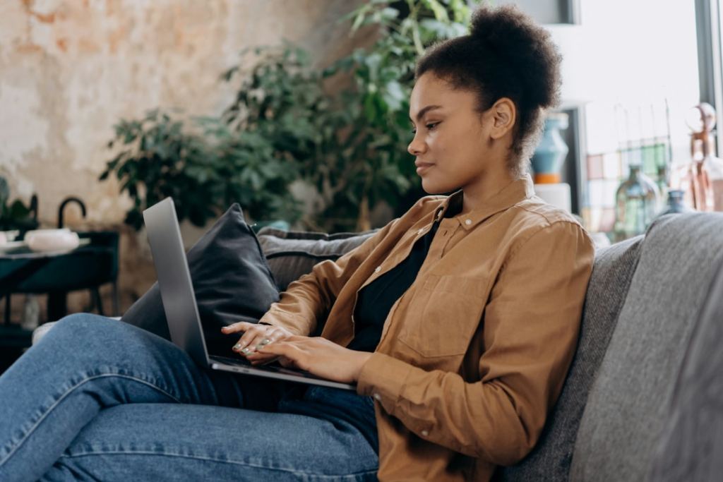 young woman sitting on couch working on latpop